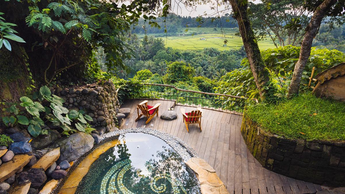 Natural spring-fed pool among lush gardens and jungle at an eco-retreat outside Ubud, Bali, with rice fields beyond