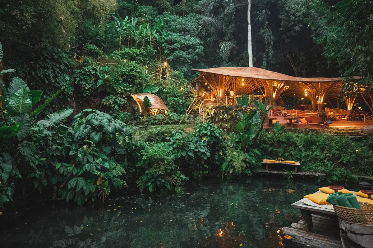 A bamboo pavilion glowing softly at dusk above a natural pool at Bambu Indah